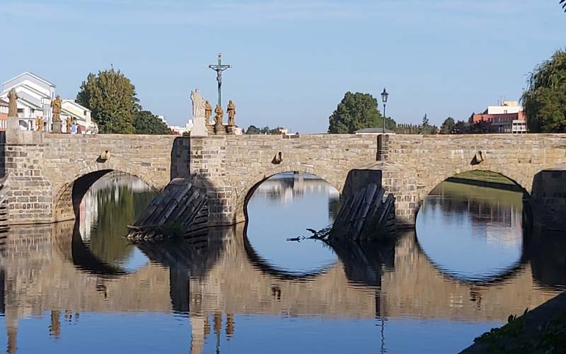 Die Steinbrücke spiegelt sich an einem sonnigen Tag im Fluß